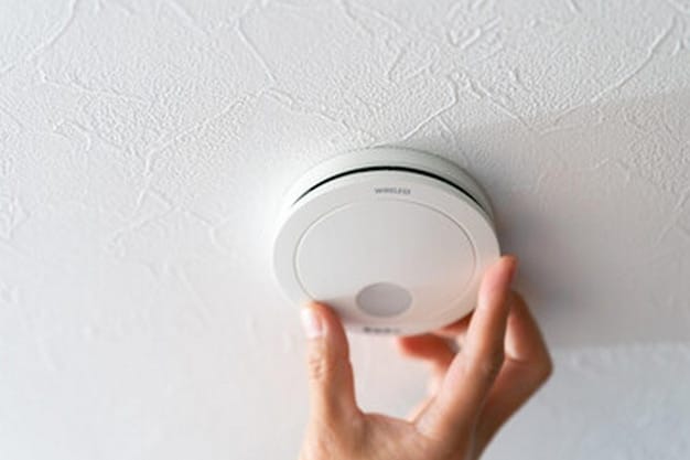 A hand holding a smart smoke detector up to a ceiling mounting bracket, about to twist and lock it into place.
