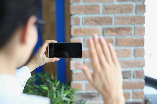 A close-up of a smart video doorbell displaying a live video feed on a smartphone. The smartphone screen shows a clear image of a person standing at the front door.