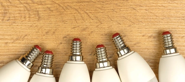 A close-up comparison of three different types of light bulbs: an incandescent bulb, a CFL bulb, and an LED bulb, highlighting their energy consumption labels and physical differences.