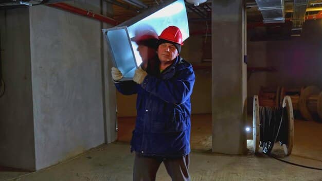 A person inspecting the insulation inside an attic. They are wearing protective gear and using a flashlight to get a better view of the coverage and condition of the insulation material.