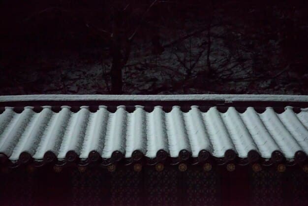 A split-screen image showing a traditional dark asphalt shingle roof on one side and a light-colored cool roof shingle roof on the other, with a thermometer indicating the temperature difference.