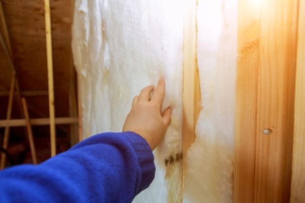 A close-up of fiberglass insulation being installed in an attic, with a worker wearing protective gear. Pay attention to the details of the insulation material, its thickness, and the surrounding wooden beams.