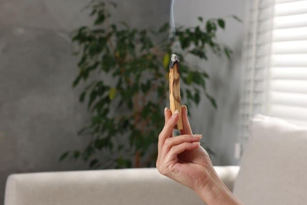 A close up shot of a hand holding an incense stick near a window frame to detect drafts, with smoke visibly being blown by escaping air.