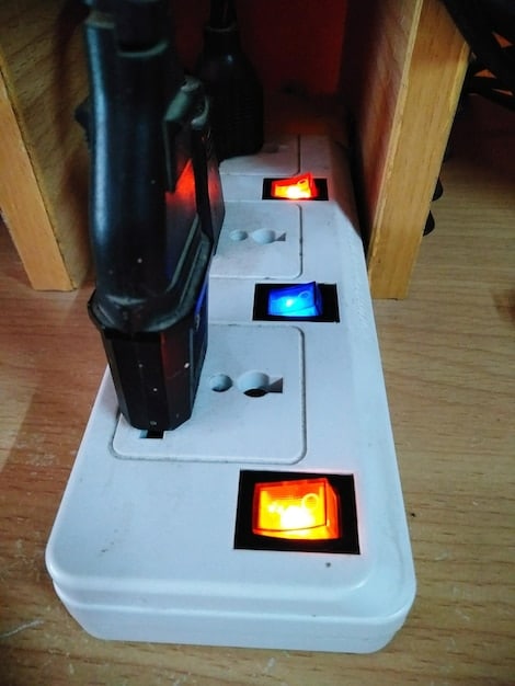 A close-up of a smart home energy monitor installed on an electrical panel, with colorful wires and circuit breakers visible. The monitor has a small display showing real-time energy consumption data.