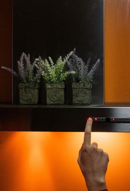 Close-up of a smart home hub device controlling lighting and sound in a home theater. The device has a touchscreen interface displaying options for pre-set scenes like 